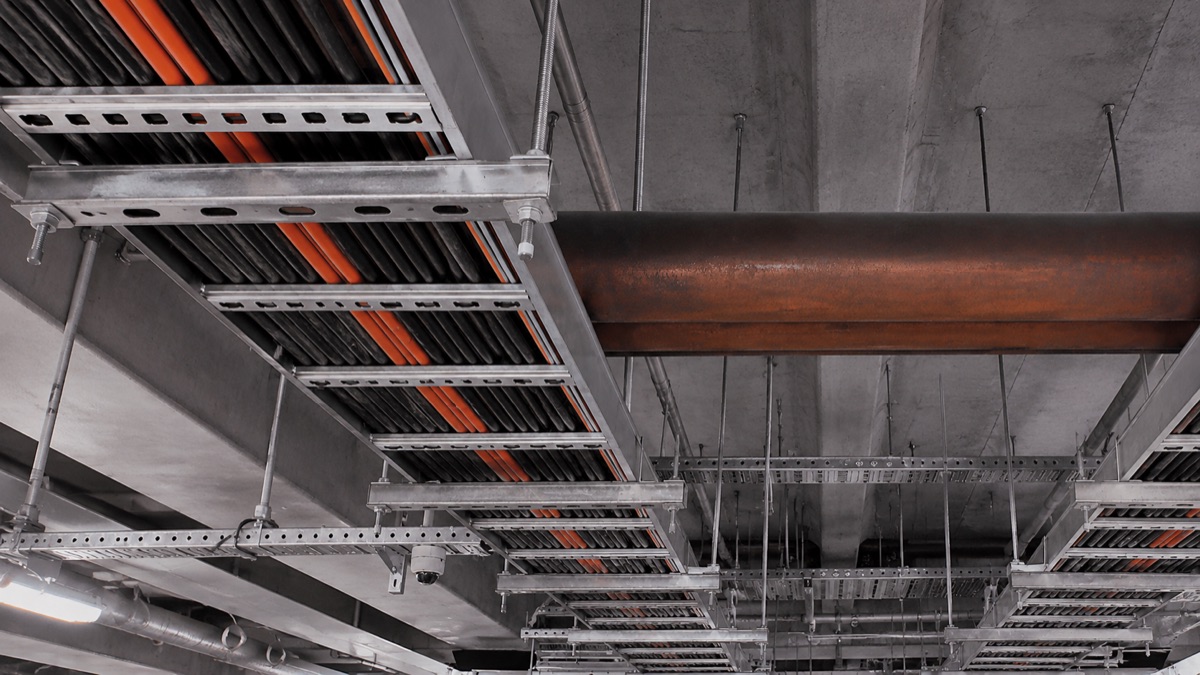 Galvanised cable ladder and perforated tray carrying armoured cables under a concrete ceiling
