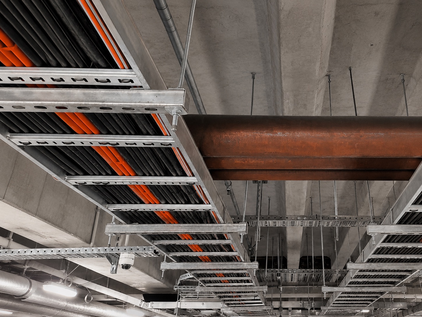Galvanised cable ladder and tray runs carrying armoured cables beneath a concrete soffit in a completed building
